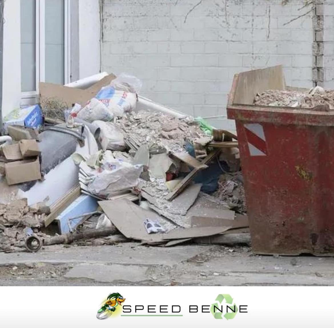 Benne &agrave; gravats rouge et tas de d&eacute;chets de chantier (DIB, pl&acirc;tre, bois) devant un immeuble en r&eacute;novation avec le logo Speed Benne.